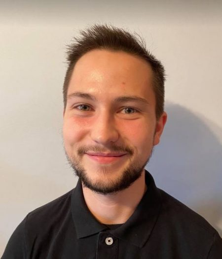 A headshot of TJ Neuhaus. He has styled short brown hair and a closely trimmed beard. He is smiling and has a cheerful look in his hazel eyes, ready to help his clients towards their goals!